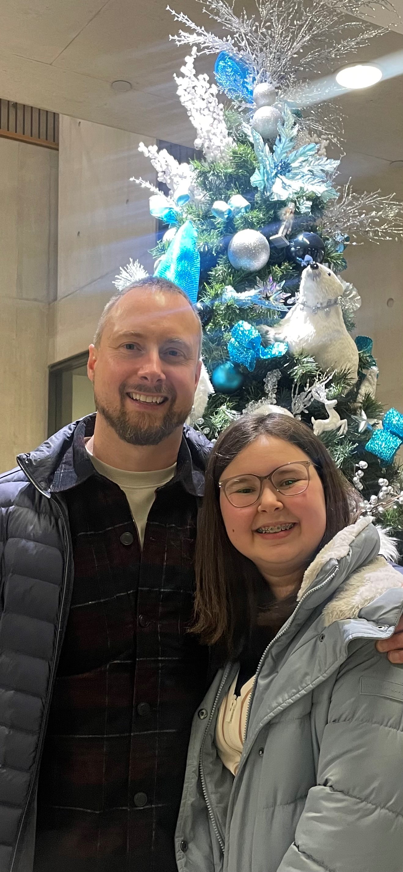 young girl and her father standing in front of a christmas tree decorated with blue and silver ornaments